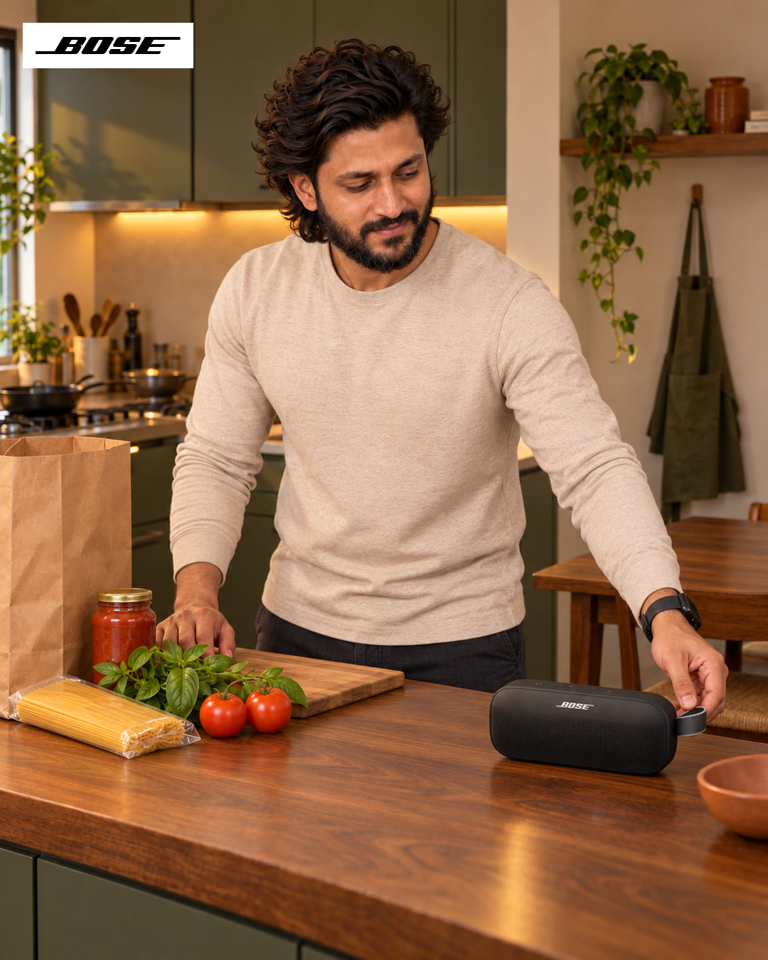 Man leaning over the counter with pasta, tomatoes and sauce, the Bose speaker within reach.