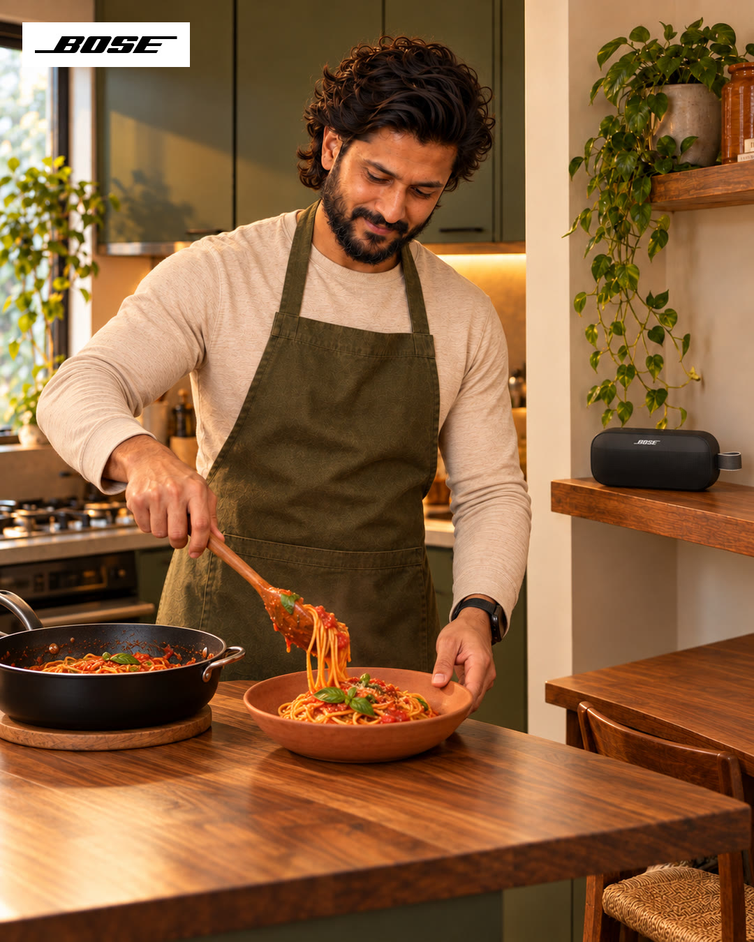Man lifting pasta from the pan with a fork, a Bose speaker on the counter.