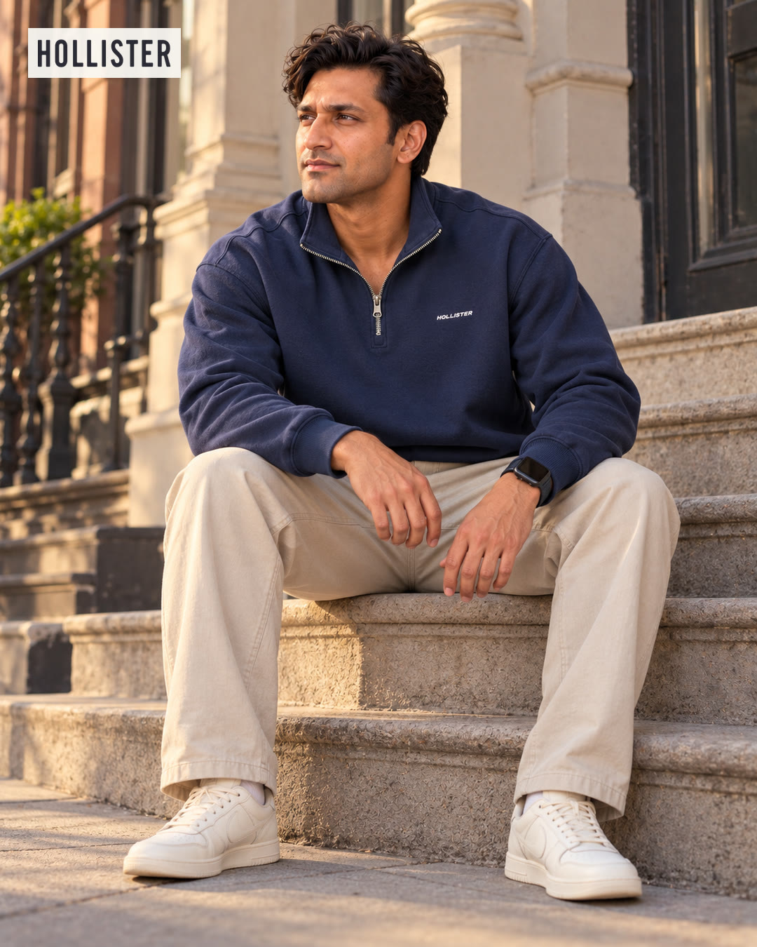 Man in a navy quarter-zip sweatshirt and khaki pants seated on stone steps, looking off to the side.