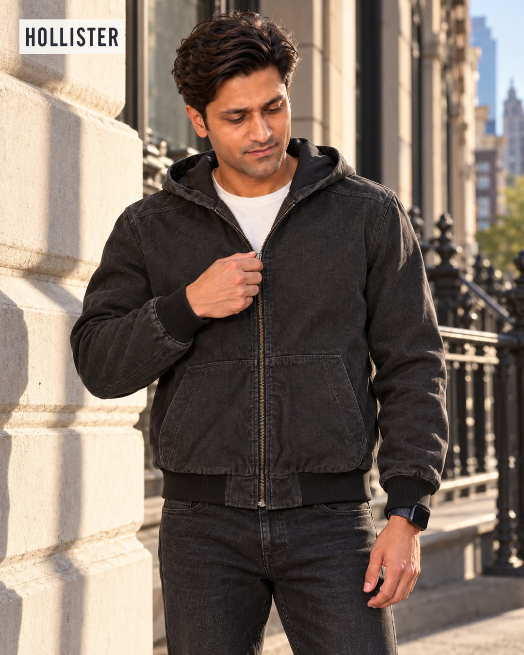 Man in a black hooded work jacket zipping it up beside a limestone wall.