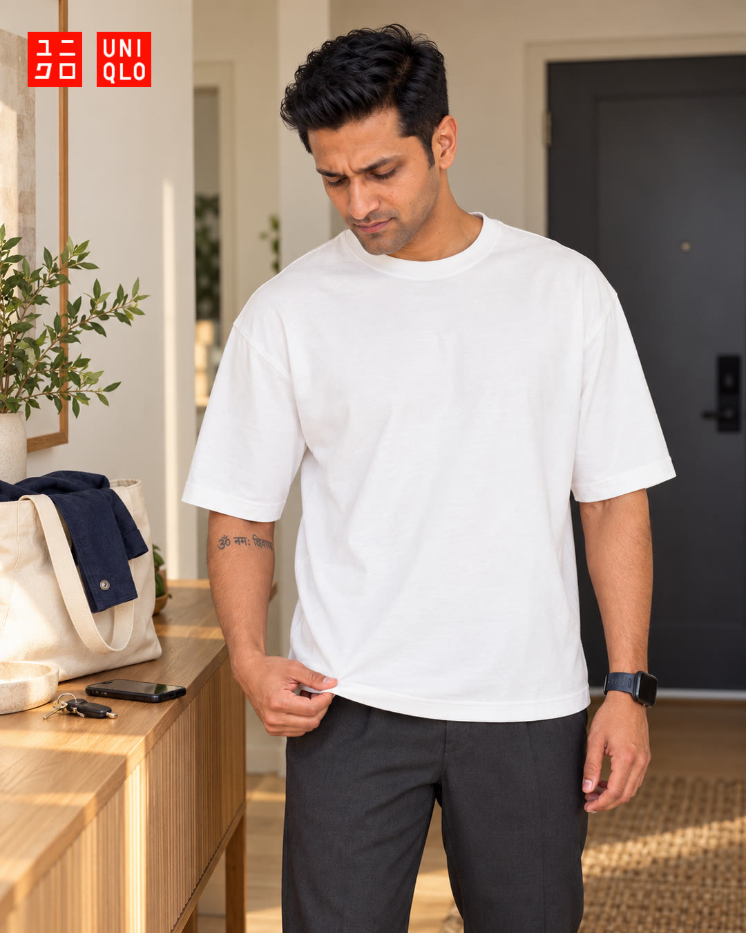 Man in a white t-shirt looking down as he tugs the hem in the entryway.