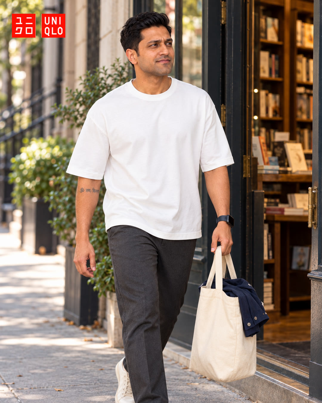 Man in a white t-shirt walking past a bookshop with a tote bag in the afternoon sun.